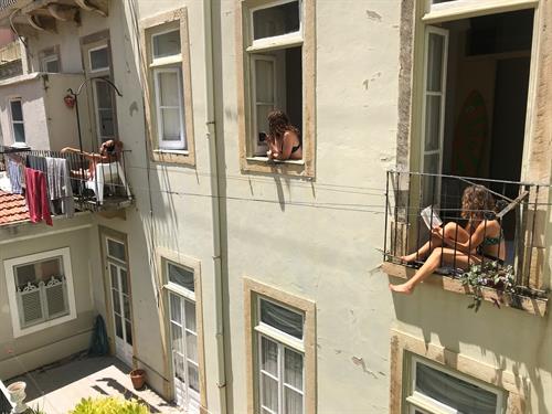 Two young women and a young man in swimwear sit in the windows of their apartments and enjoy the sun during the corona-induced lockdown in Lisbon.